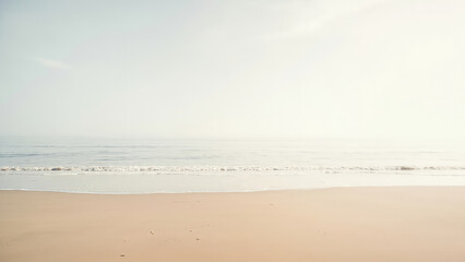 Sandy beach with gentle waves meeting the shore under a hazy sky serene coastal landscape with soft colors and a tranquil atmosphere
