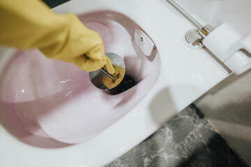 Gloved hand scrubbing a toilet with a cleaning brush. A detailed view of maintaining hygiene and...