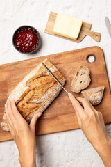 Hands cutting bread, preparing bread with butter and strawberry jam
