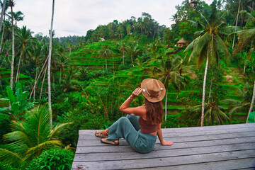 Happy carefree woman traveler wearing hat enjoying landscape of picturesque green rice terraces in...