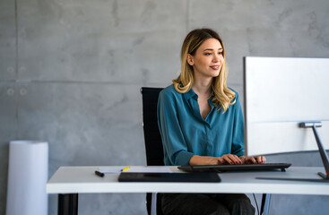 Young happy successful business woman working with computer in corporate office