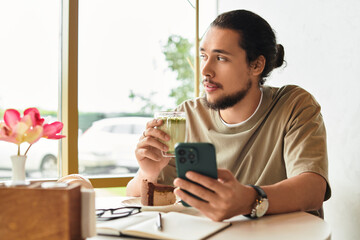 Charming young man enjoying matcha and cake while using smartphone in a cozy summer cafe