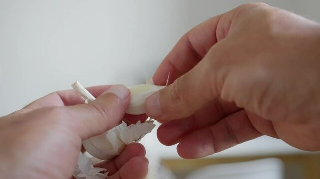 Closeup of hands skillfully peeling a garlic bulb, ideal for various culinary projects and food preparation. slow motion