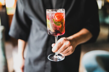 Close-up of a hand holding a refreshing fruit cocktail with strawberries, lime, and mint in a clear glass, perfect for summer parties, bars, and lifestyle concepts.