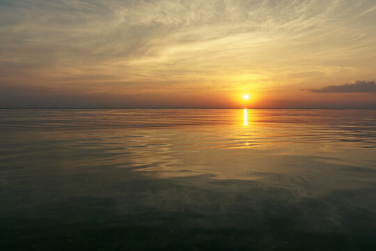 Beautiful sunset over the ocean with soft waves and glowing sky in warm yellow, orange, and red tones. Peaceful seascape evoking calm, romance, and evening serenity.