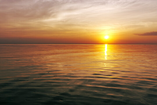 Beautiful sunset over the ocean with soft waves and glowing sky in warm yellow, orange, and red tones. Peaceful seascape evoking calm, romance, and evening serenity.