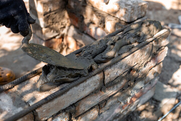 applying wet cement to brick structure showing texture and process of barbecue construction,...