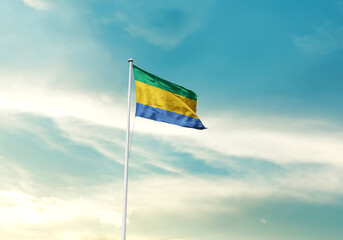 Gabon flag is waving on a tall flagpole among the clouds. Gabon national flag for independence day.