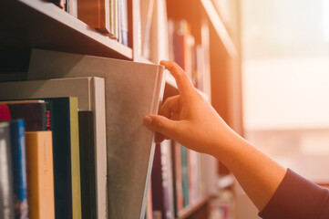 Hand picking a book or takes out from the shelf, pulling book from bookshelf in public library in...
