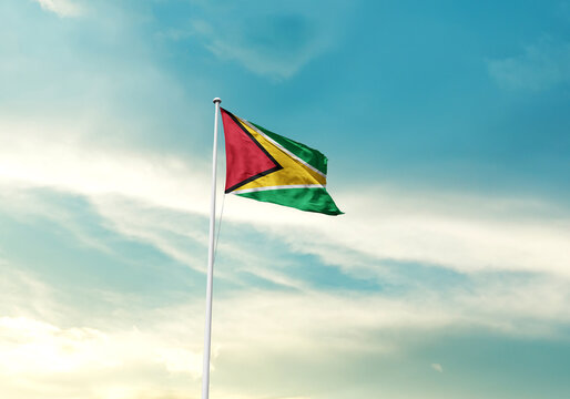 Guyana flag is waving on a tall flagpole among the clouds. Guyana national flag for independence day. - Powered by Adobe