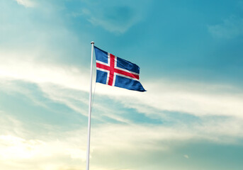 Iceland flag is waving on a tall flagpole among the clouds. Iceland national flag for independence day.