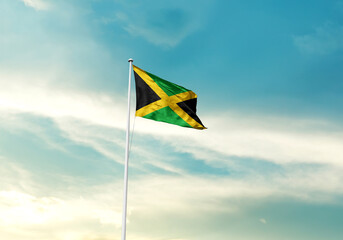 Jamaica flag is waving on a tall flagpole among the clouds. Jamaica national flag for independence...