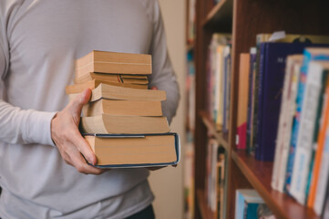 Young man holding  books in library, closeup, Man hands holding book from bookshelf in public...