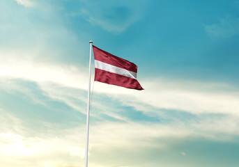 Latvia flag is waving on a tall flagpole among the clouds. Latvia national flag for independence day.