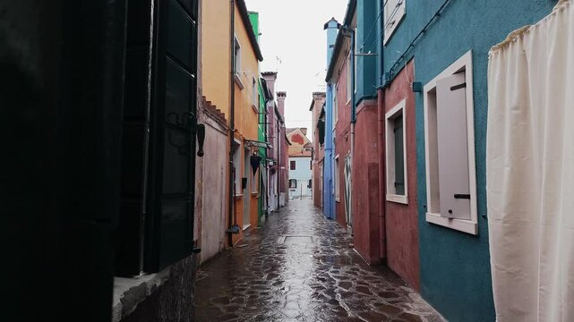 Slides shot reveals narrow empty wet paved street with painted houses