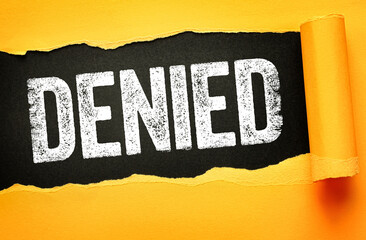 DENIED in bold, distressed white text on a dark black background revealed through torn yellow paper. Concept of rejection, refusal, blocked access, disapproval, failure, or decline