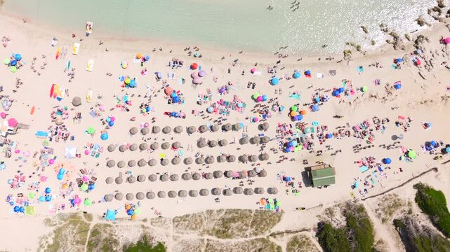 Tourists sunbathe on crowded beach with colorful umbrellas in Mallorca, aerial birds eye