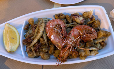 Close-up of assorted seafood including shrimp being grilled in a pan. Golden crust, appetizing texture, and rich colors suggest a flavorful and freshly cooked meal.