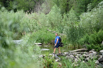 Obraz premium A man crosses a river on rocks with a backpack.