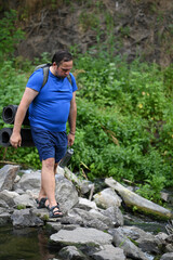 A man crosses a river on rocks with a backpack.