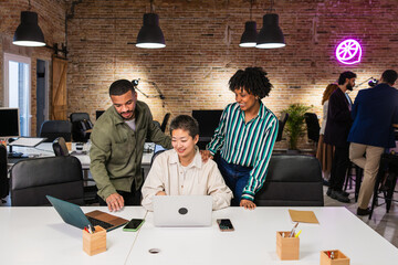 Multi ethnic team collaborating on laptop in modern office