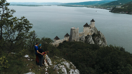 Couple and two dogs enjoy a scenic viewpoint overlooking Golubac Fortress and the Danube River....