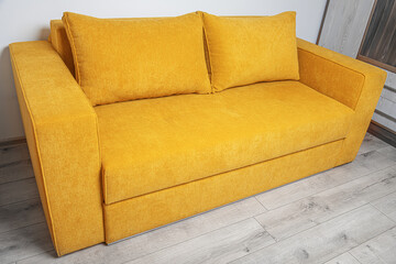 A modern yellow fabric sofa with two large cushions is placed in a bright, minimalistic living room...