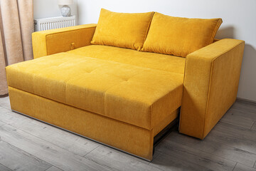 A modern yellow fabric sofa with two large cushions is placed in a bright, minimalistic living room...