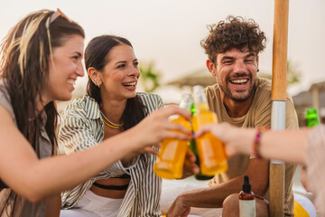 Friends toasting with bottles of juice on the beach at sunset
