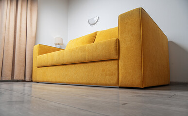 A modern yellow fabric sofa with two large cushions is placed in a bright, minimalistic living room...