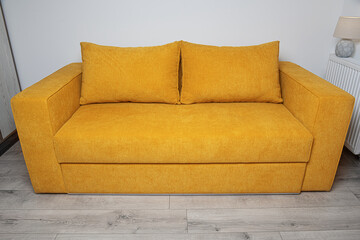 A modern yellow fabric sofa with two large cushions is placed in a bright, minimalistic living room...