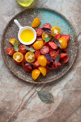 Plate with fresh strawberry, mixed tomato and basil salad on a brown granite background, vertical shot with space, above view