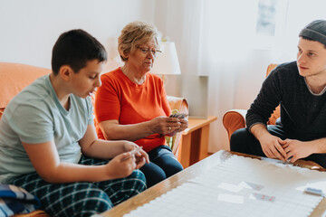 A joyful scene of a grandmother and two family members bonding over a card game at home, creating...