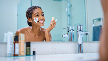 Woman applying skincare cream on face in bathroom mirror, showing beauty, health, wellness routine. Skincare Routine concept.