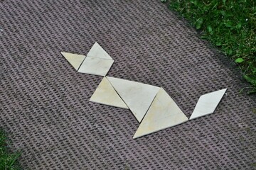 Creative arrangement of wooden tangram pieces forming a cat figure on textured outdoor mat....