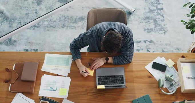 Above, laptop and businessman writing on sticky note for planning, strategy and ideas for proposal. Office, startup and person with documents and computer for research, online project and reminder