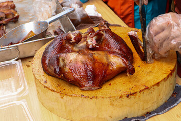 A whole roasted duck with glossy, crispy brown skin rests on a large wooden chopping block, ready...