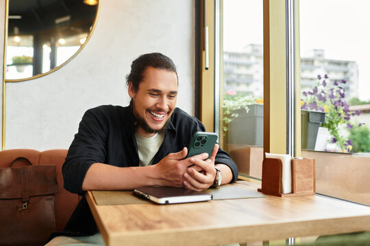 Young man with beard enjoys remote work in bustling cafe during a sunny summer day