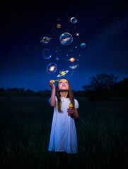 Girl in field blowing bubbles at night