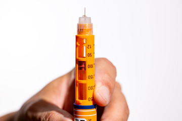 Man Holding Orange Insulin Pen Upright with Needle on White Background © Emre