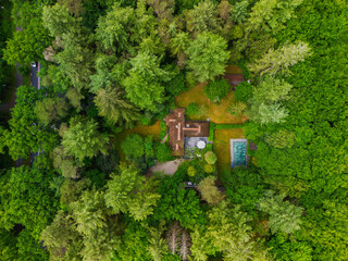 A peaceful house hidden deep in the forest, surrounded by lush green trees and nature. The drone...