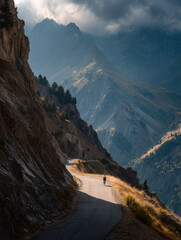 Cyclist climbing a steep alpine road at sunset, dramatic mountain scenery.