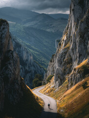 Cyclist climbing a steep alpine road at sunset, dramatic mountain scenery.
