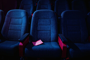 Obraz premium Torn movie ticket stub on empty theater seat in dark lighting 