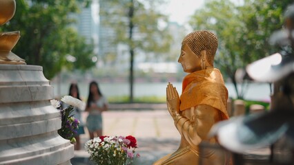 Golden buddha statue with flowers in a peaceful outdoor setting