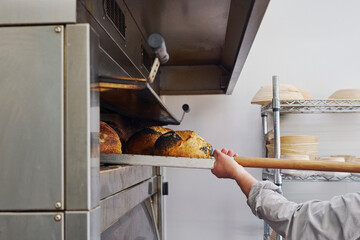 Close Up Of Male Baker Taking Sourdough Loaves Out Of Oven With Paddle In Bakery