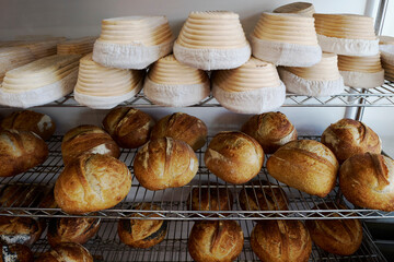 Freshly baked sourdough loaves cooling on racks in bakery with banneton baskets for proving above