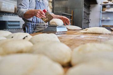 Close up of baker cutting and weighing batch of dough to make individual loaves in bakery