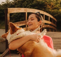 Close-up of a woman hugging a Welsh Corgi in the park in sunny weather. Concept of walking a dog,...