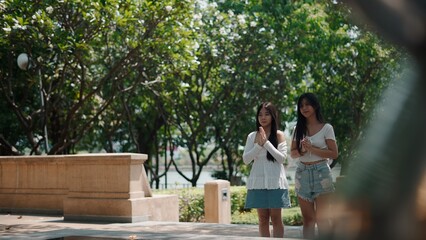 Tourists joining hands, praying together in thai park, demonstrating cultural reverence and...